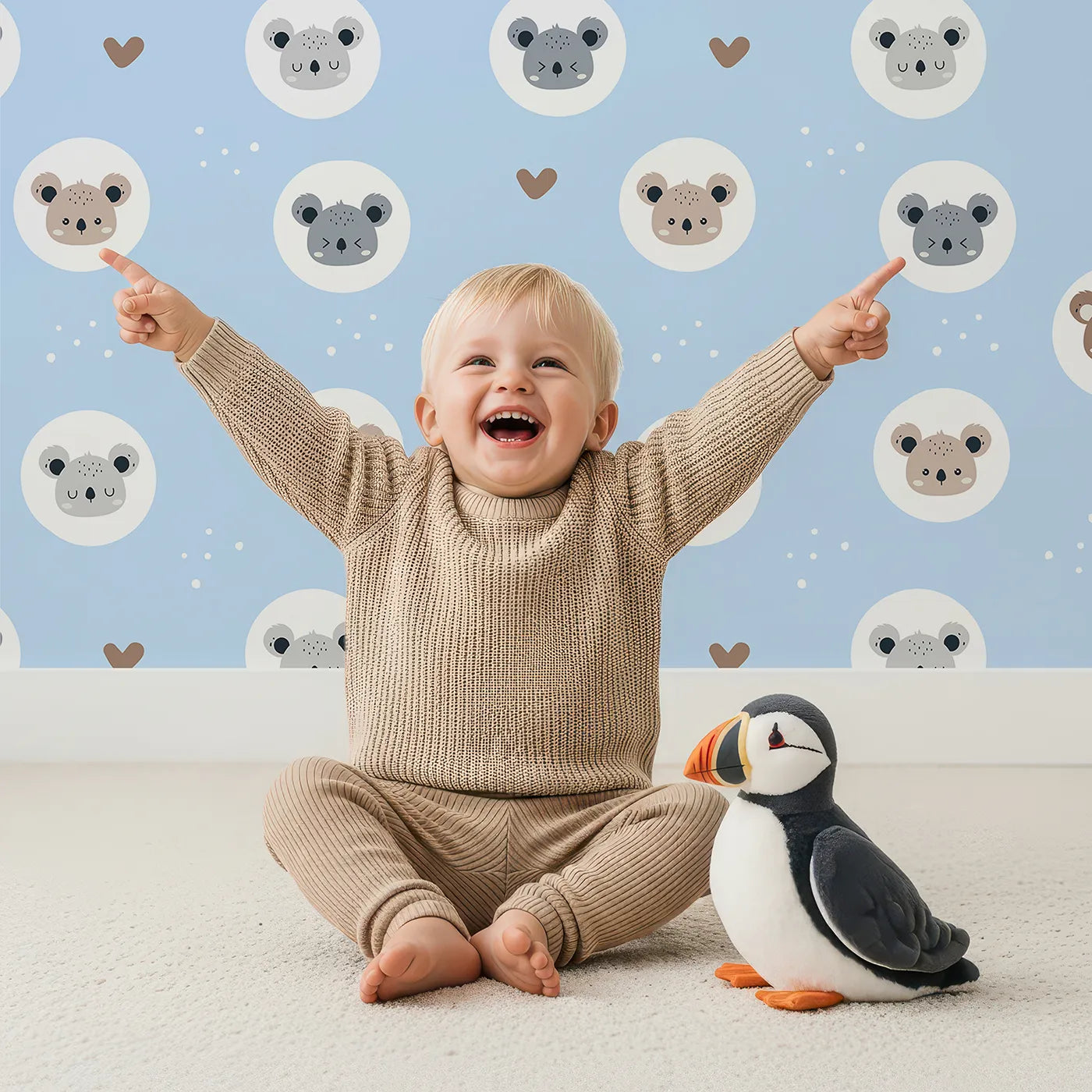 Lovely child standing in front of Whimsy Tots Cuddly Koala Circle Wallpaper in Sky Blue with koala, heart, circle, dot, face in design.