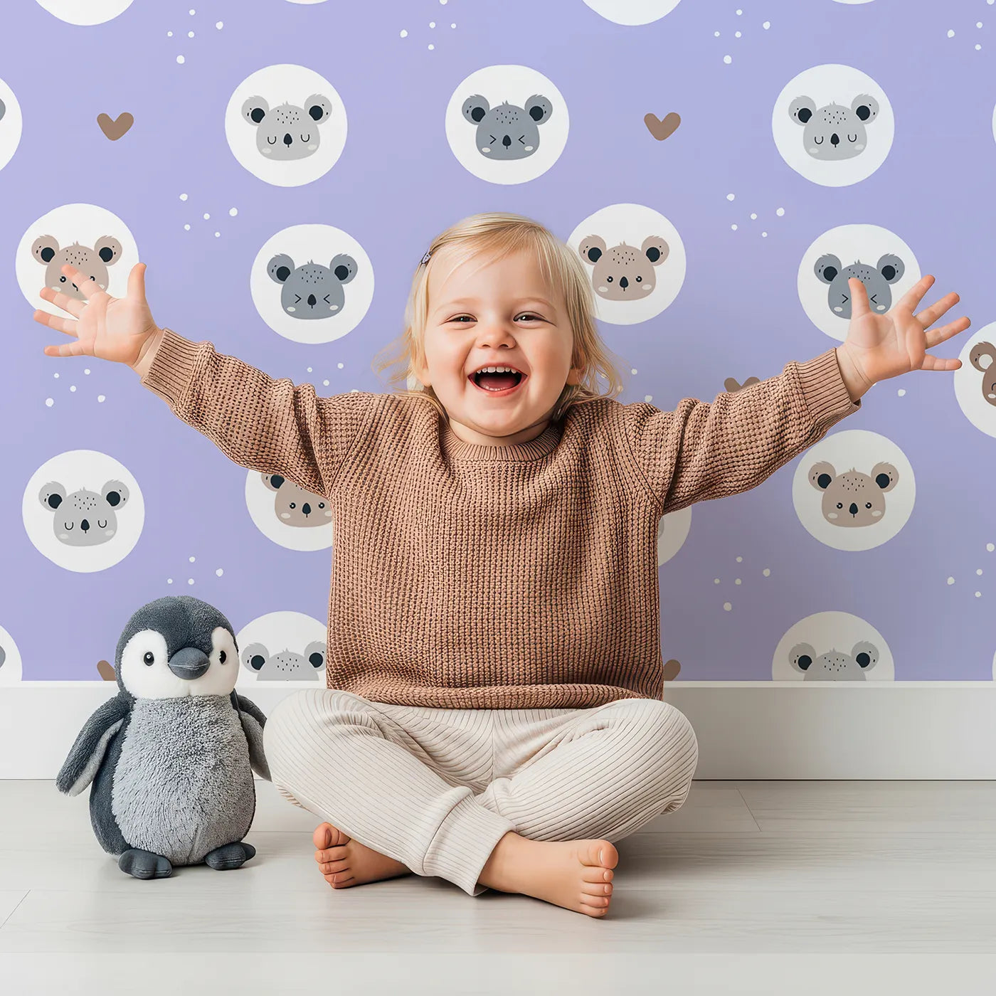 Lovely child standing in front of Whimsy Tots Cuddly Koala Circle Wallpaper in Lavender Mist with koala, heart, circle, dot, face in design.