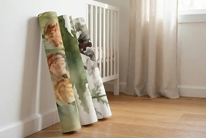Three premium rolls of woven peel and stick wallpaper with a watercolor pine tree pattern leaning against a nursery wall.