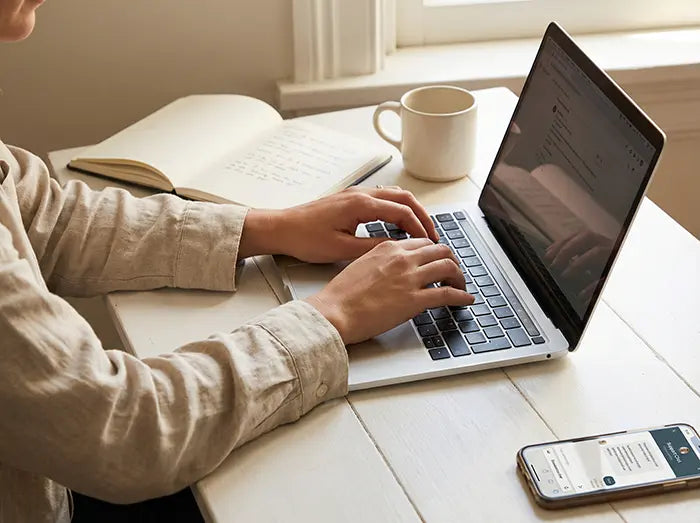 Whimsy Tots support team member working at a sunny home desk, typing on a laptop to assist parents with returns and exchanges.